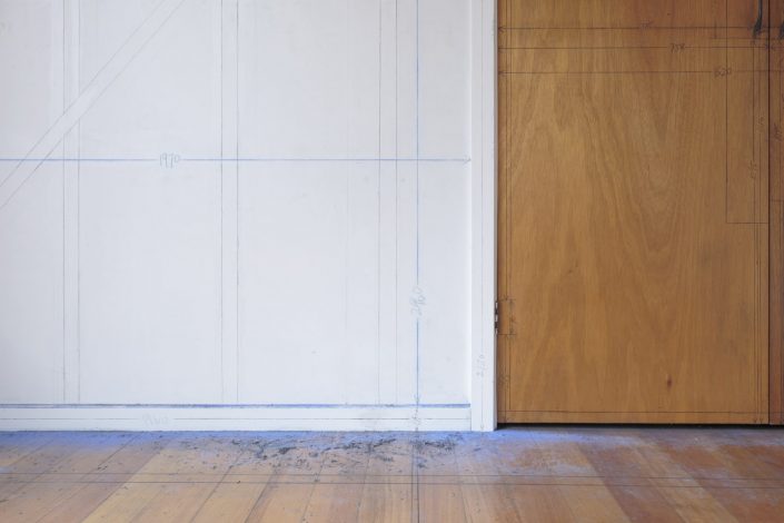 Documentation of drawing installation that used black pencil and blue chalk stringlines to trace the timber structure of a room in a suburban house. Detail view of floor, cupboard and shirting board.