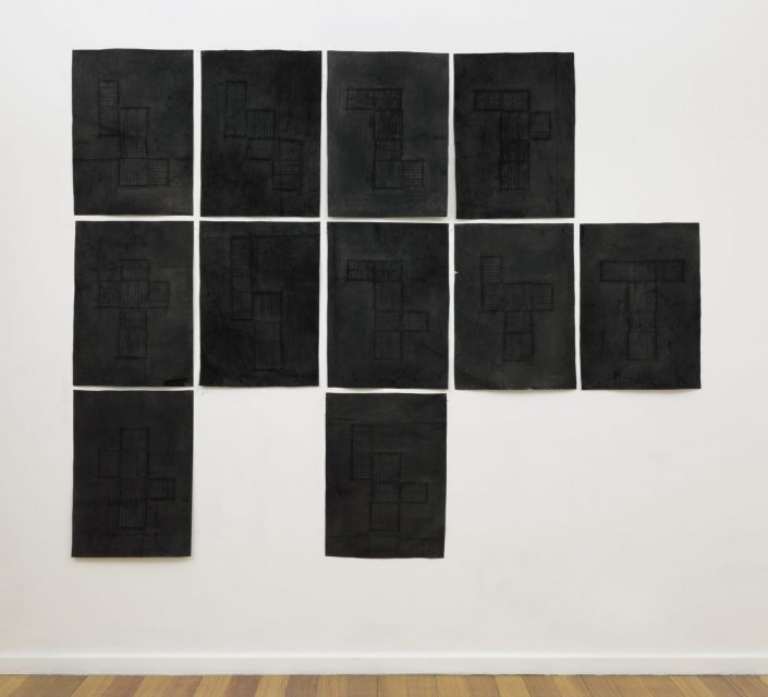 Series of velvety black charcoal rubbings arranged in a partial grid depicting the 11 ways a 3 dimensional model of the room can be flattened onto a two dimensional surface.