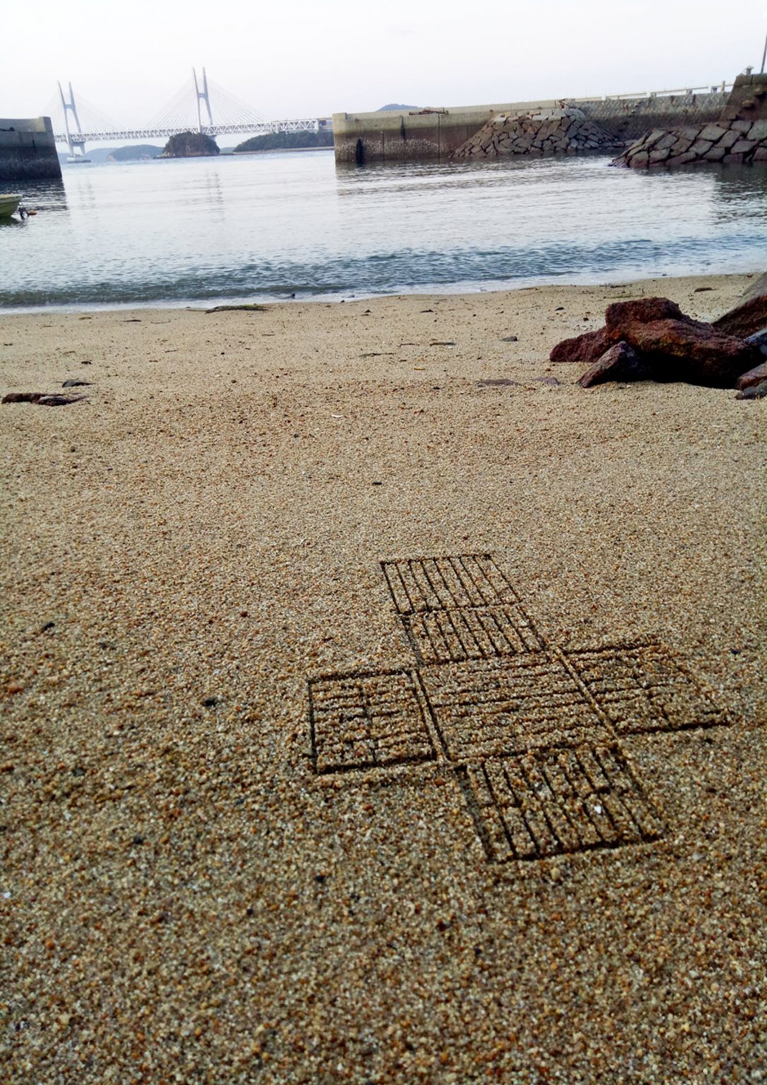 A geometric pattern embedded in the sand of an island beach at the water's edge.