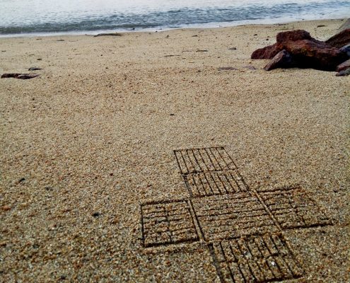 A geometric pattern embedded in the sand of an island beach at the water's edge.